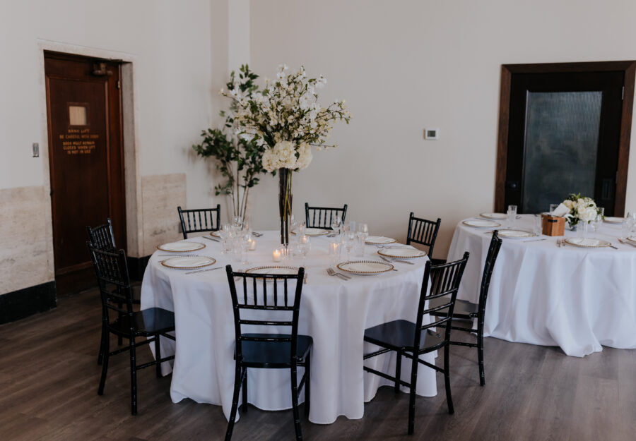 Round reception tables with white linens, black chairs, and tall floral centerpieces at The Reserve a Grand Venue.