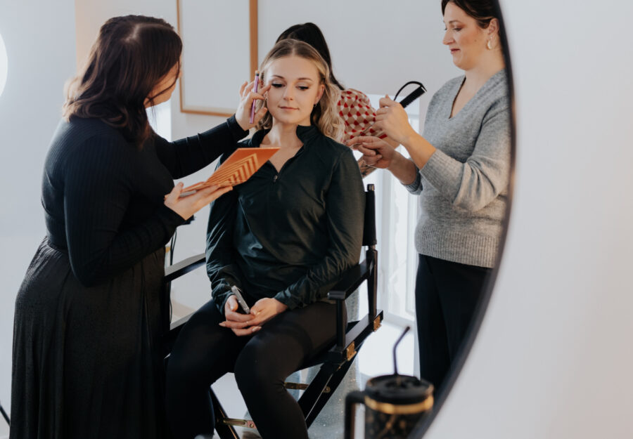 Makeup artist applying finishing touches while bride sits in preparation chair before the wedding.