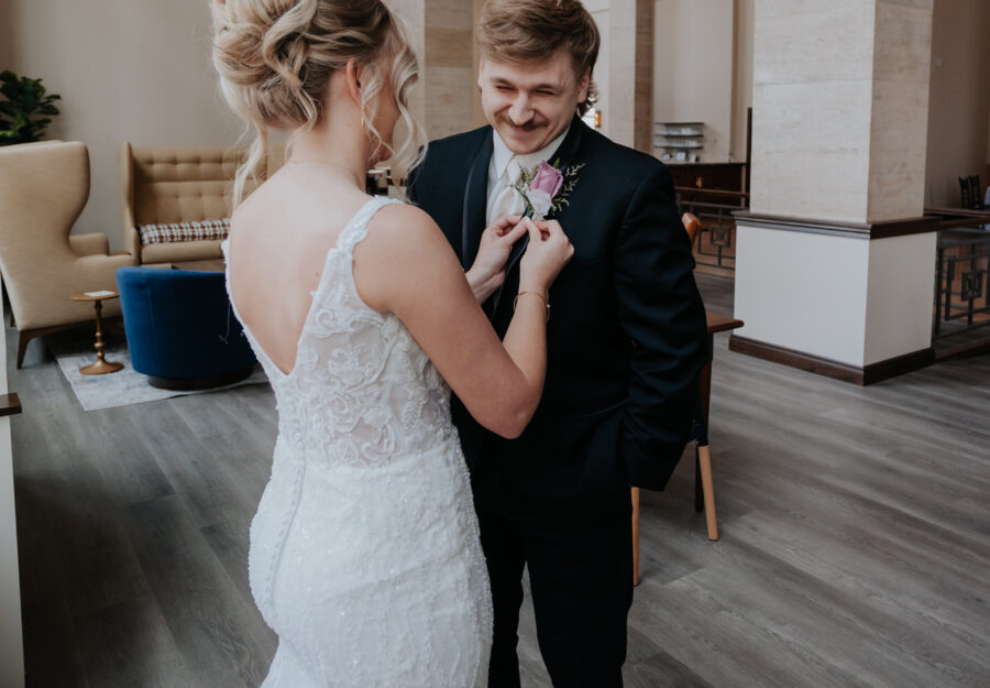Bride adjusting the groom’s boutonniere during a romantic wedding moment inside The Reserve.