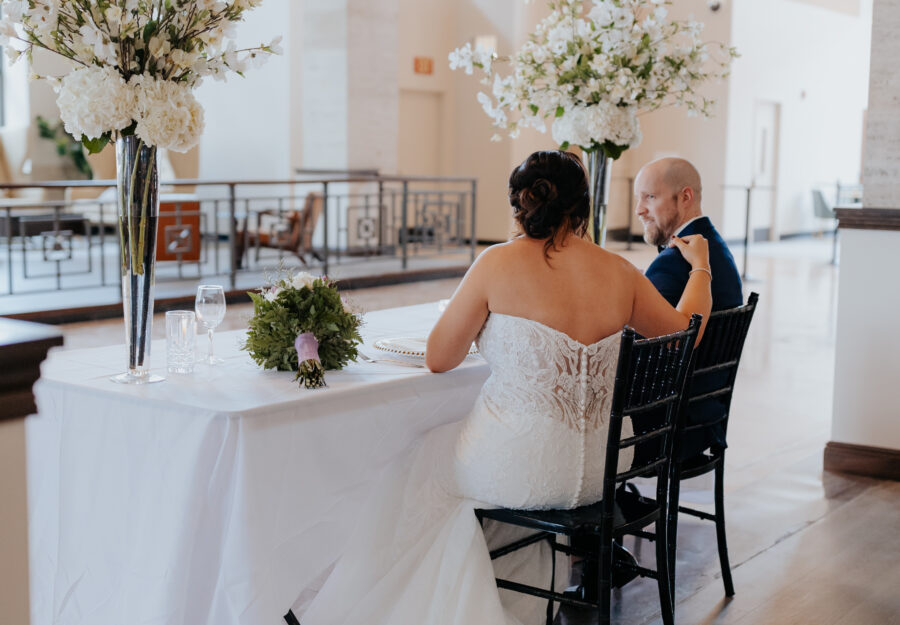 Bride and groom seated at reception table surrounded by tall floral arrangements in The Reserve a Grand Venue